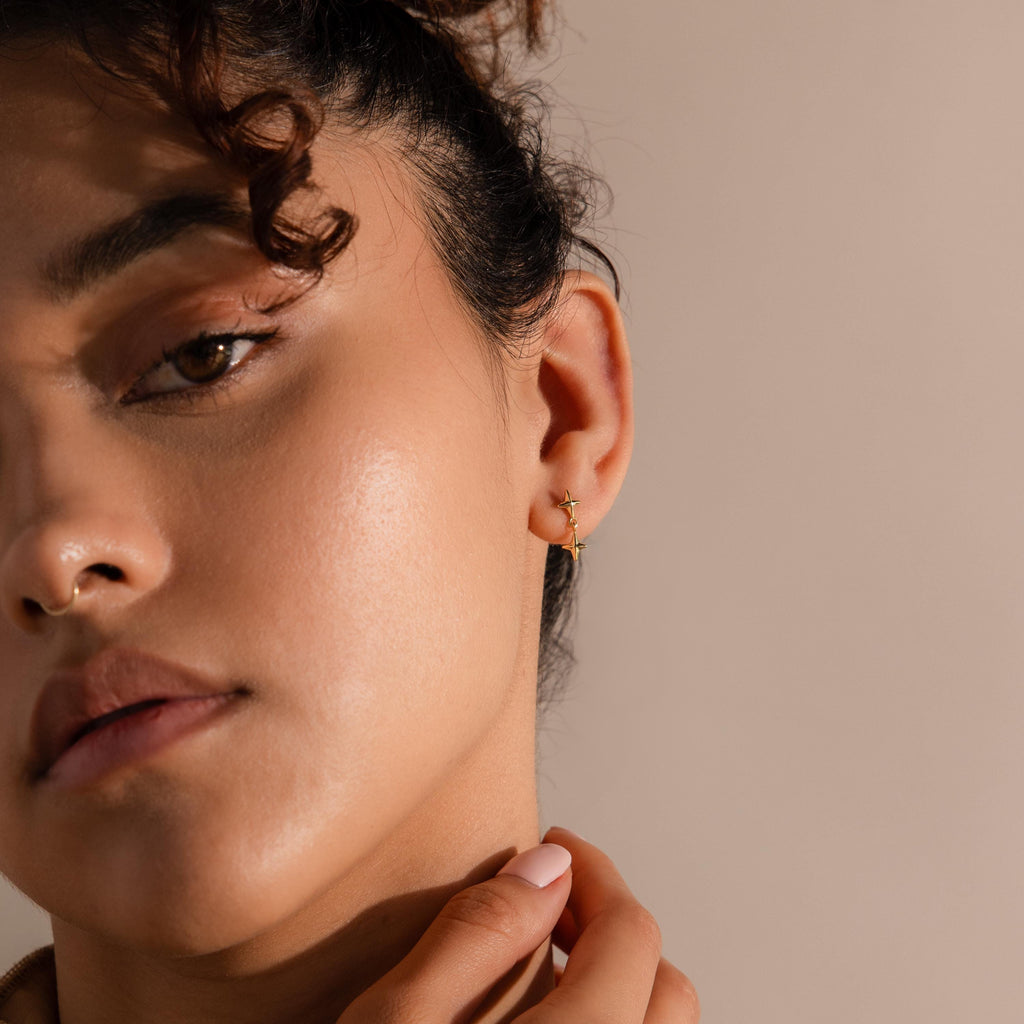 Close-up of a person with curly hair wearing small gold hoops and touching their neck, styled with Star Drop Flatback Studs as delicate cartilage earrings for a subtle celestial jewelry look.