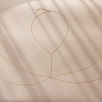 Gold body chain laid flat on a soft beige surface with shadow lines.