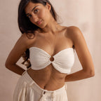 Woman wearing a gold body chain styled through the center of a white bandeau top, layered gracefully along her waist with pleated cream pants.