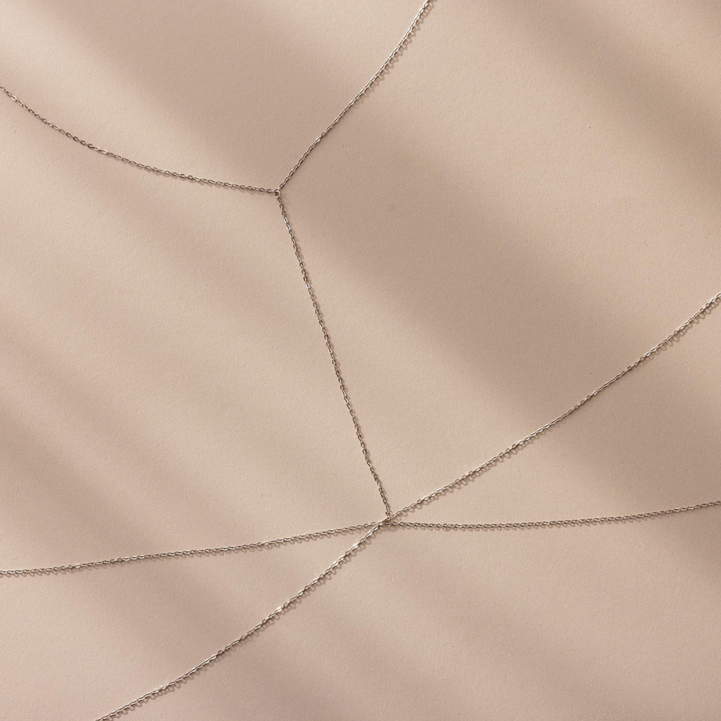 Close-up of silver body chain overlapping in delicate layers on a neutral background.