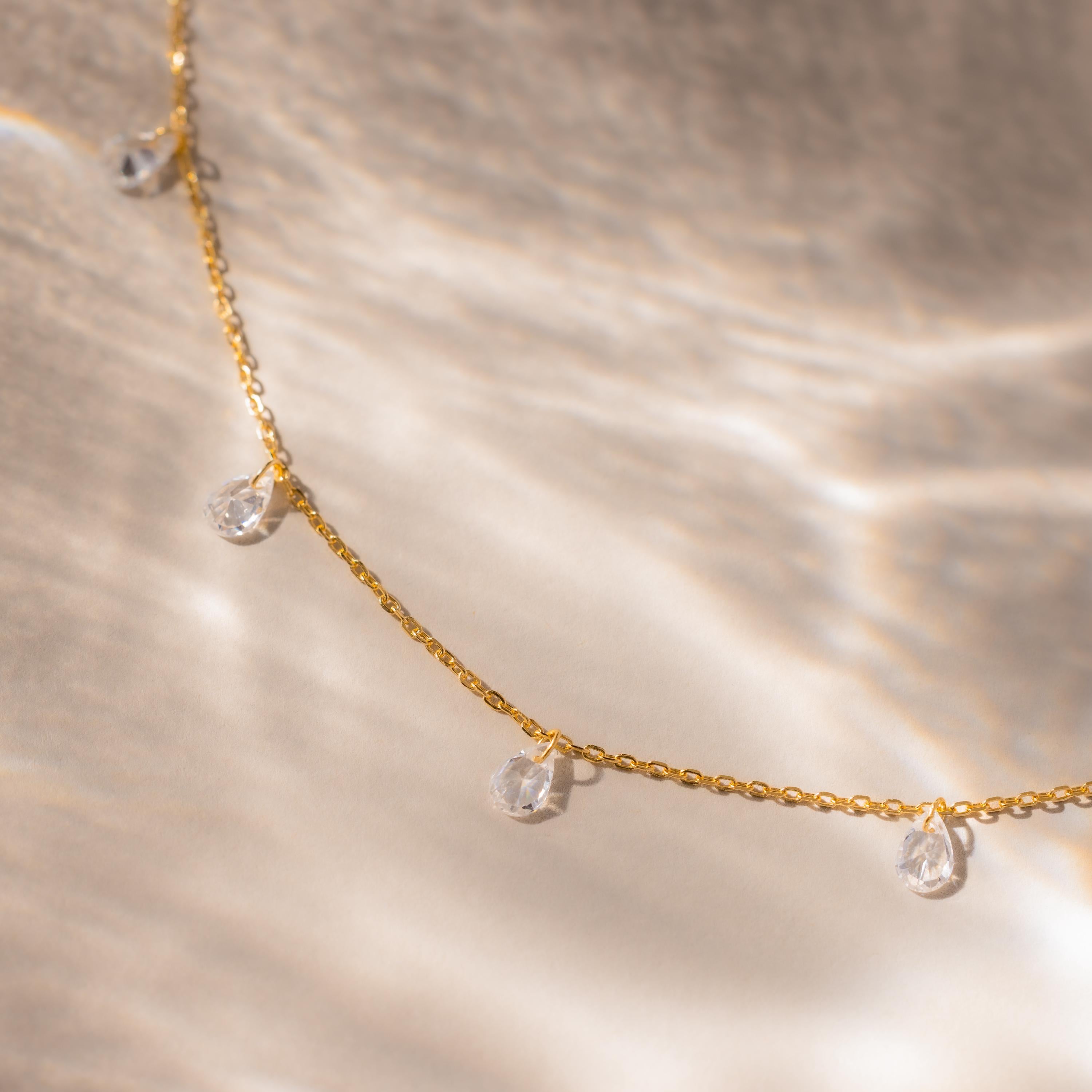 Close-up of the gold teardrop necklace laid flat on a neutral surface with soft lighting.