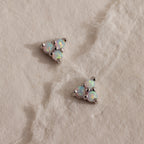 A pair of silver Opal Cluster Stud Earrings resting on a white textured paper, with a triangular trio of luminous white opals set in polished silver.