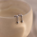 A pair of silver flat back earrings with double star drops hanging from a smooth, curved ceramic surface