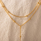 Close-up of the necklace’s gold satellite bead chain against a textured cream background.