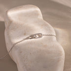 Delicate silver chain bracelet displayed on a textured stone surface, featuring an interlocking oval link design with one link encrusted in small clear stones.