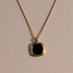 Gold chain necklace featuring a square black onyx pendant in a textured gold bezel, displayed against a neutral background with soft lighting.