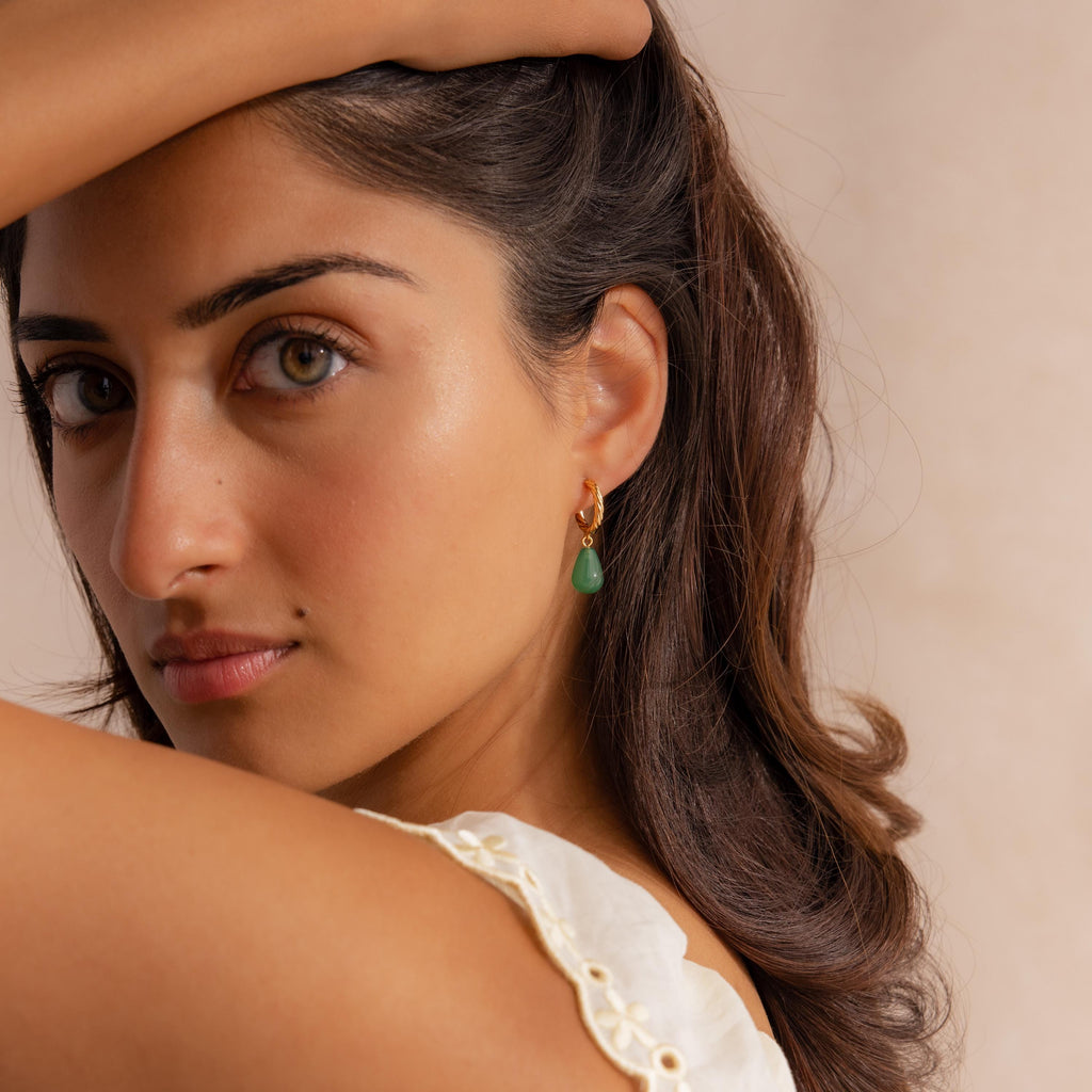 Woman with wavy brown hair wearing Twisted Jade Hoops and a white top, arm raised above her head.