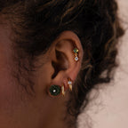 Close-up of a woman’s ear adorned with multiple earrings, highlighting a green carved jade rose stud with a sparkling center stone.