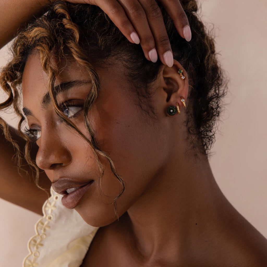 Side profile of a model wearing a dark green jade rose stud earring with a crystal center, styled alongside gold and gemstone ear cuffs and hoops.