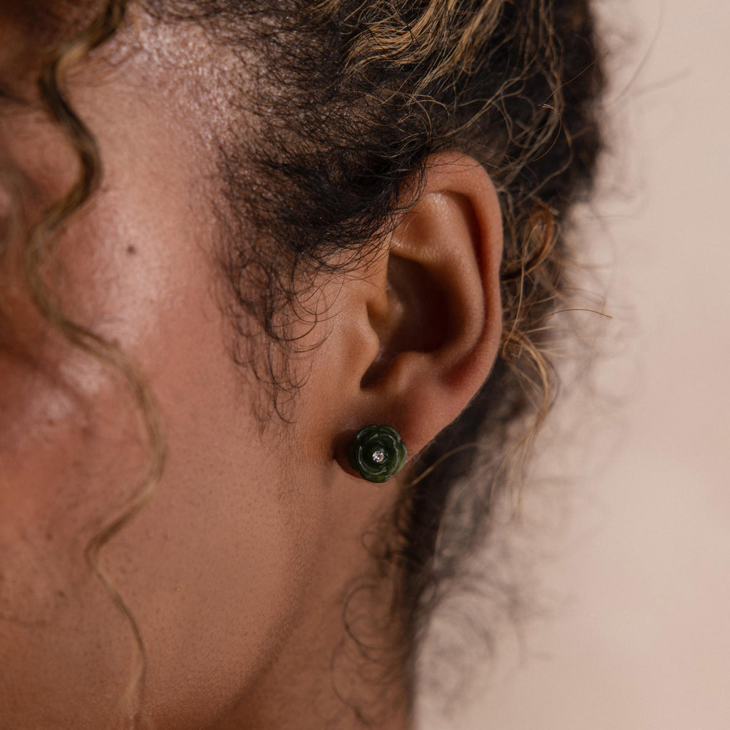 Close up of a woman wearing a green jade rose stud earring, styled with soft curls.