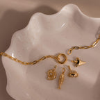 The Crab Charm features on a gold chain with four ocean-themed charms, elegantly displayed on a wavy ceramic dish—perfect beach jewelry to complement your seaside-inspired style.
