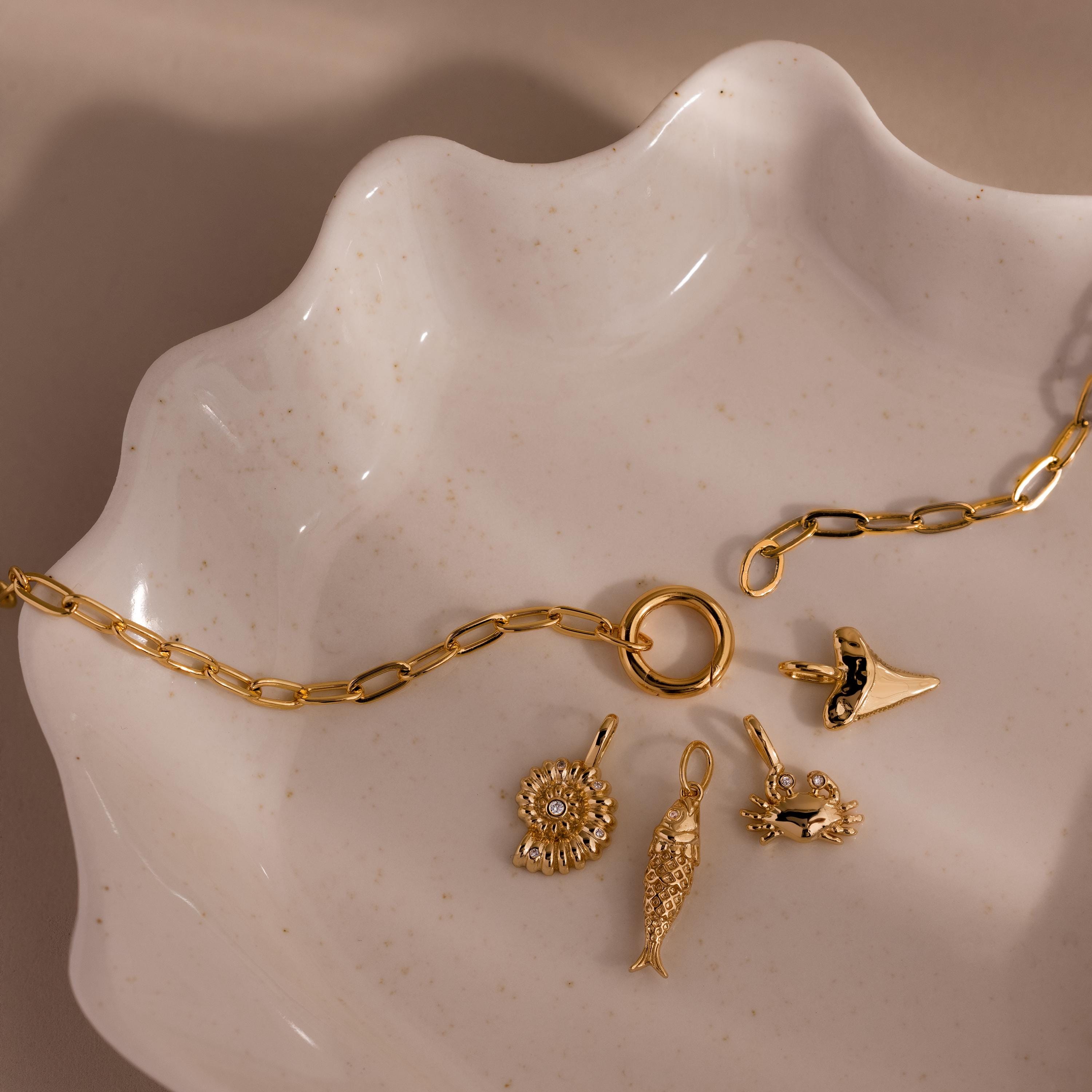 The Crab Charm features on a gold chain with four ocean-themed charms, elegantly displayed on a wavy ceramic dish—perfect beach jewelry to complement your seaside-inspired style.