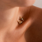 Close-up of a woman's collarbone adorned with two gold charms, a detailed crab charm and a polished shark tooth charm, both catching the light against bare skin.