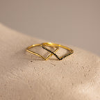 Two gold chevron rings displayed on a textured surface, one plain and one accented with pavé-set black stones.