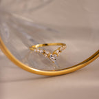 Gold heart curve cluster diamond ring with heart shaped center stone and round diamonds displayed against a reflective glass surface.