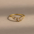 Delicate gold ring with a row of tapered baguette and marquise cut clear gemstones set in a subtle curved design, creating a refined and elegant look.