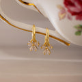 Gold Starlight Bow Hoop earrings with dangling baguette cut clear stones arranged in a bow design, displayed hanging from a porcelain handle with floral detail.