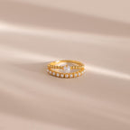 Gold beaded ring set featuring one band with a single central pearl and another adorned with a row of small pearls, displayed on a neutral beige surface with soft light shadows.