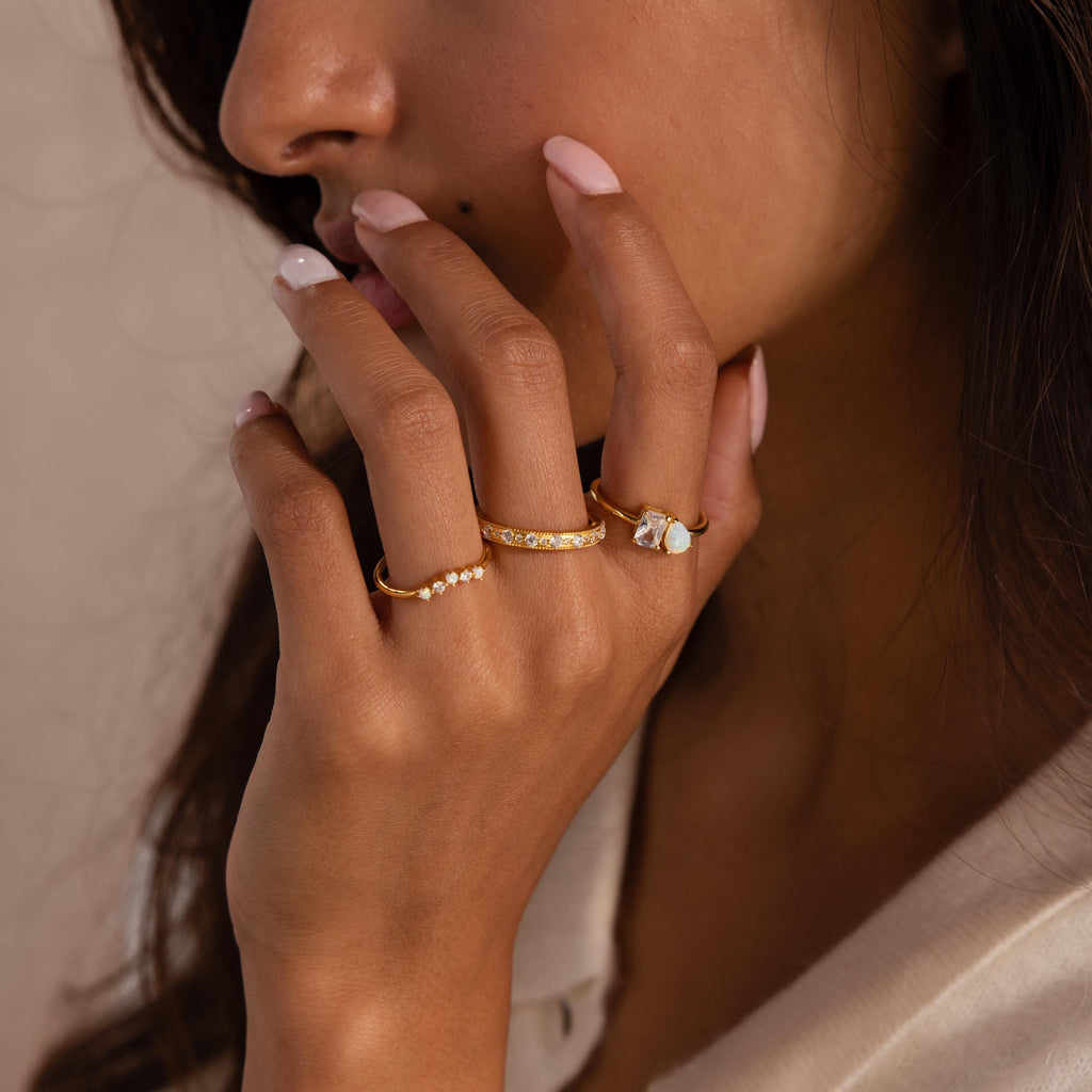A woman’s manicured hand wears three gold rings: one with pearls, another with a flower design, and the striking Opal Diamond Toi et Moi Ring.