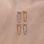 Four Bow Chain Studs in gold and silver feature delicate chain accents. Displayed on beige fabric, these feminine, vintage-inspired earrings are a charming jewelry addition.