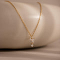 Butterfly Drop Necklace, featuring three small sparkling diamonds, is displayed on a smooth beige surface—an elegant piece of nature-inspired jewelry.