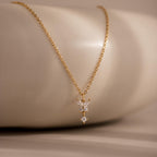 Butterfly Drop Necklace, featuring three small sparkling diamonds, is displayed on a smooth beige surface—an elegant piece of nature-inspired jewelry.