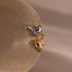 Gold and silver crab shaped charm pendants with gemstone-accented eyes, displayed on a smooth stone surface against a neutral background.