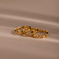 Set of three gold eternity curve rings with quilted wave design, including one with diamond accents, displayed on a soft neutral surface.