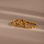 Set of three gold eternity curve rings with quilted wave design, including one with diamond accents, displayed on a soft neutral surface.