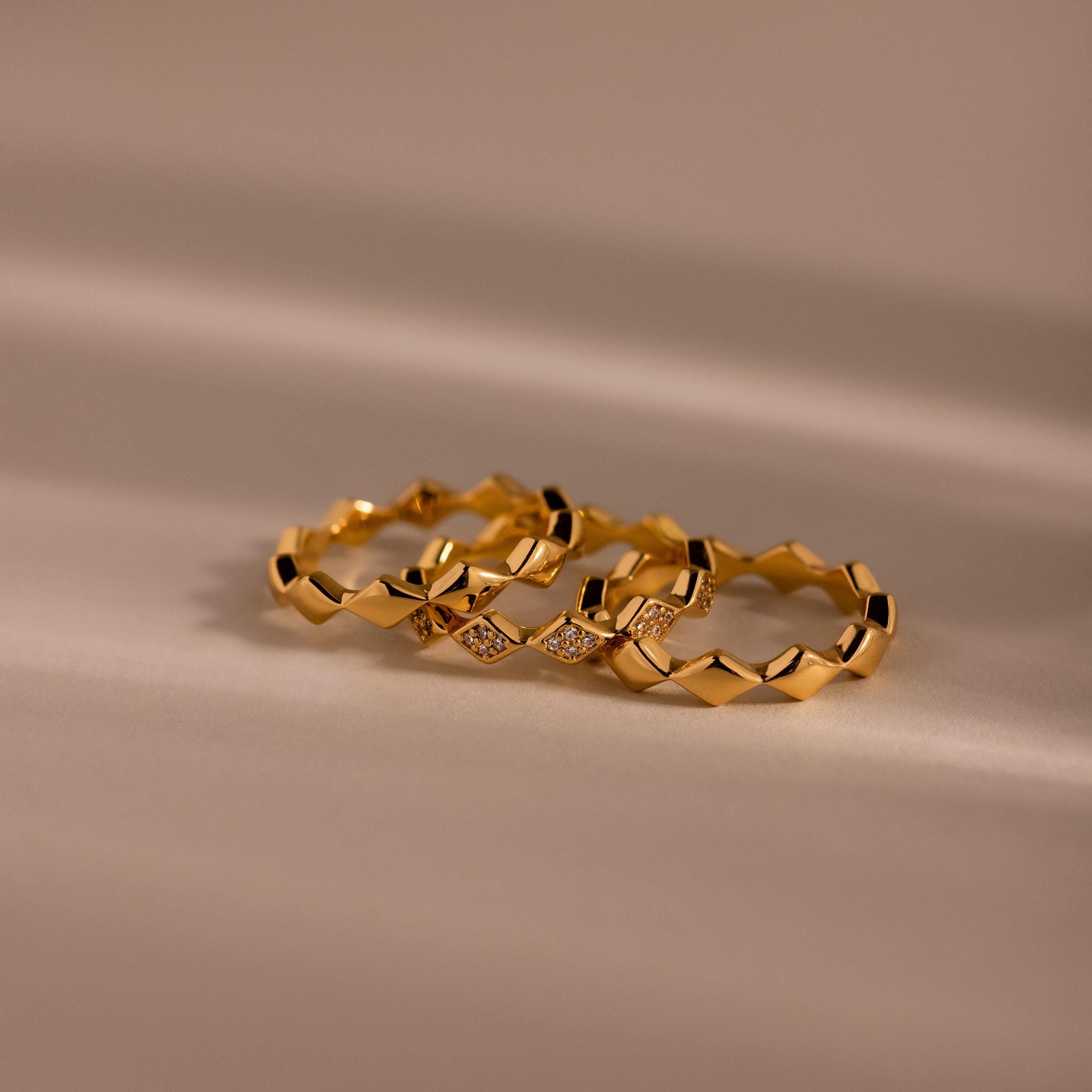 Set of three gold eternity curve rings with quilted wave design, including one with diamond accents, displayed on a soft neutral surface.