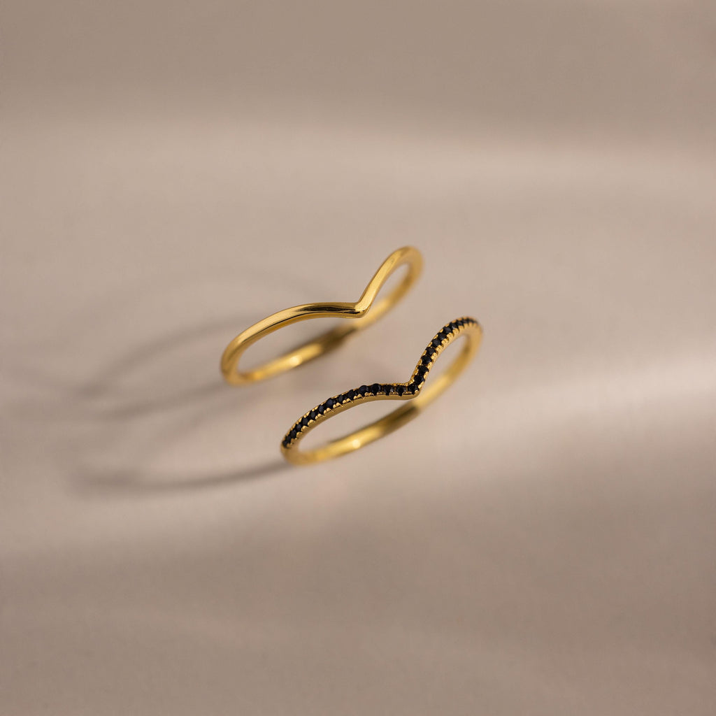 Set of two gold curve rings, one with a smooth polished band and the other accented with black pavé stones, displayed on a neutral background.