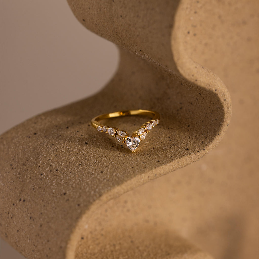 Gold heart curve cluster diamond ring with a heart shaped center stone and round diamonds displayed on a textured stone surface.