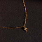 Gold chain bracelet featuring a sparkling crystal cross charm, photographed against a dark textured background for a bold and elegant presentation.