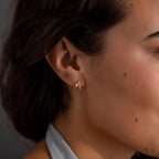 Close-up of a woman's ear wearing elegant earrings—a small gold letter A stud—paired with Pave Diamond Duo Huggies, her hair tucked behind her ear.