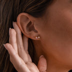 A woman's ear is adorned with Marquise Onyx & Pearl Studs, featuring a striking gold design; her hand is gently poised near her elegant earrings.