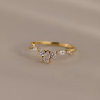Radiant Tear Ring in polished gold with a pear cut diamond center framed by round and marquise side stones, displayed on a soft neutral background.