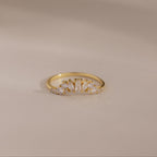 The Diamond Curve Cluster Ring features an baguette stone and a row of clear marquise and round diamonds set in gold, displayed on a smooth, neutral surface.