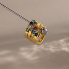The Multiple Birthstone Band in 18K Gold features four stacked gold rings set with colorful square gemstones, creating a stunning personalized jewelry piece against a neutral background.