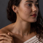 Woman with wavy hair wears the Jade Bar Jewelry Set in Sterling Silver, featuring a silver necklace and small green stud earrings, as she looks to the side.