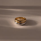 The Mixed Metal Dome Ring Set features a gold and silver ring intertwined, resting on a smooth beige surface with soft shadows—a versatile and modern classic jewelry piece.