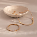 The 3-Prong Diamond Tennis Necklace & Bracelet Set with clear gemstones is displayed on a beige surface next to a ceramic bowl.