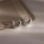 The Bold Teardrop Earrings, with their shiny silver finish, rest on a light, reflective surface—ideal for anyone who loves modern jewelry.