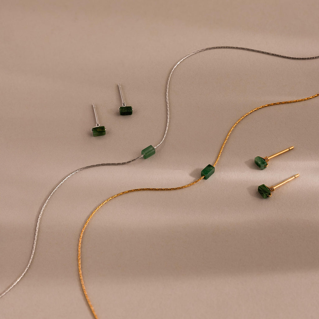 The Jade Bar Jewelry Set, featuring two pairs of jade stud earrings and two matching bar necklaces, is elegantly displayed on a beige background.