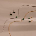 The Jade Bar Jewelry Set, featuring two pairs of jade stud earrings and two matching bar necklaces, is elegantly displayed on a beige background.