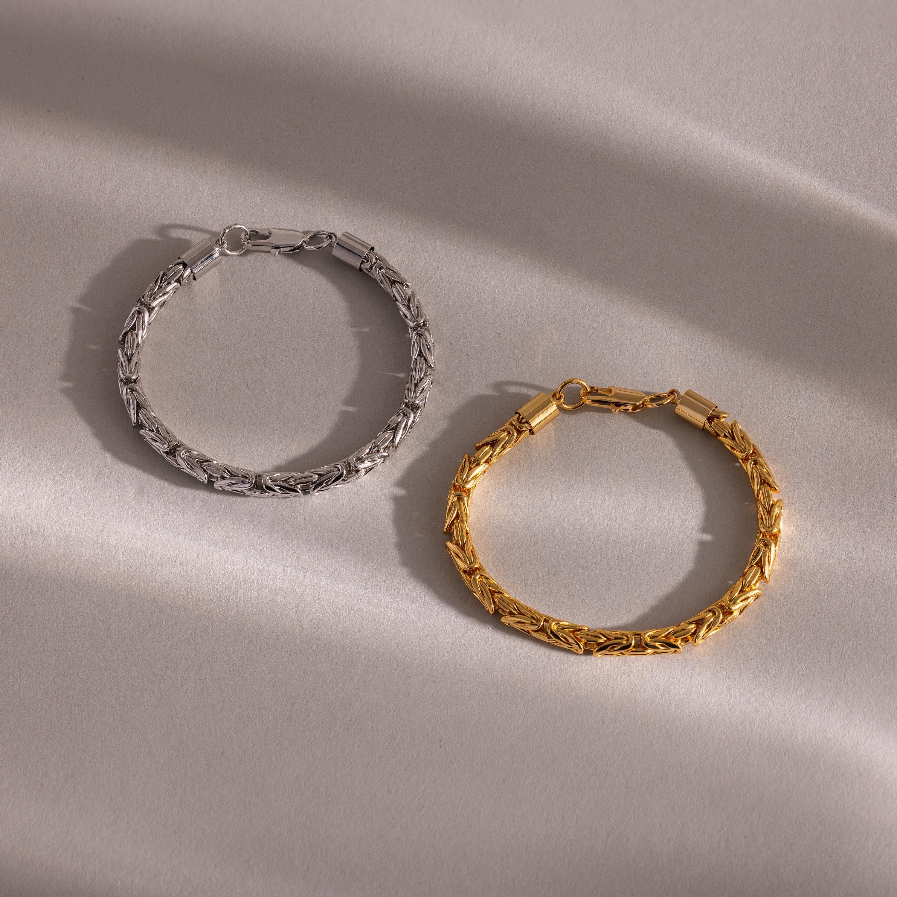 The Byzantine Link Bracelet, crafted in silver and gold with an interwoven design, rests on a light textured surface with soft shadows, showcasing statement jewelry inspired by classic Byzantine style.