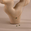 The Jade Bar Jewelry Set, featuring a gold necklace with a green jade stone and matching stud earrings, is displayed on a beige abstract textured stand.