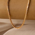 The Diamond Bezel Tennis Necklace & Bracelet Set features round bezel-set diamonds against a beige textured background, ideal for elegant pairings.