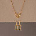 The Linked Charm Necklace and Earrings Set features two interlocking heart-shaped links and matching gold earrings, making an elegant anniversary gift displayed on a beige background.