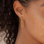 Close-up of a person wearing a gold rectangular link earring from the Linked Charm Necklace and Earrings Set in 18K Gold, with curly hair visible—an elegant choice for an anniversary gift.