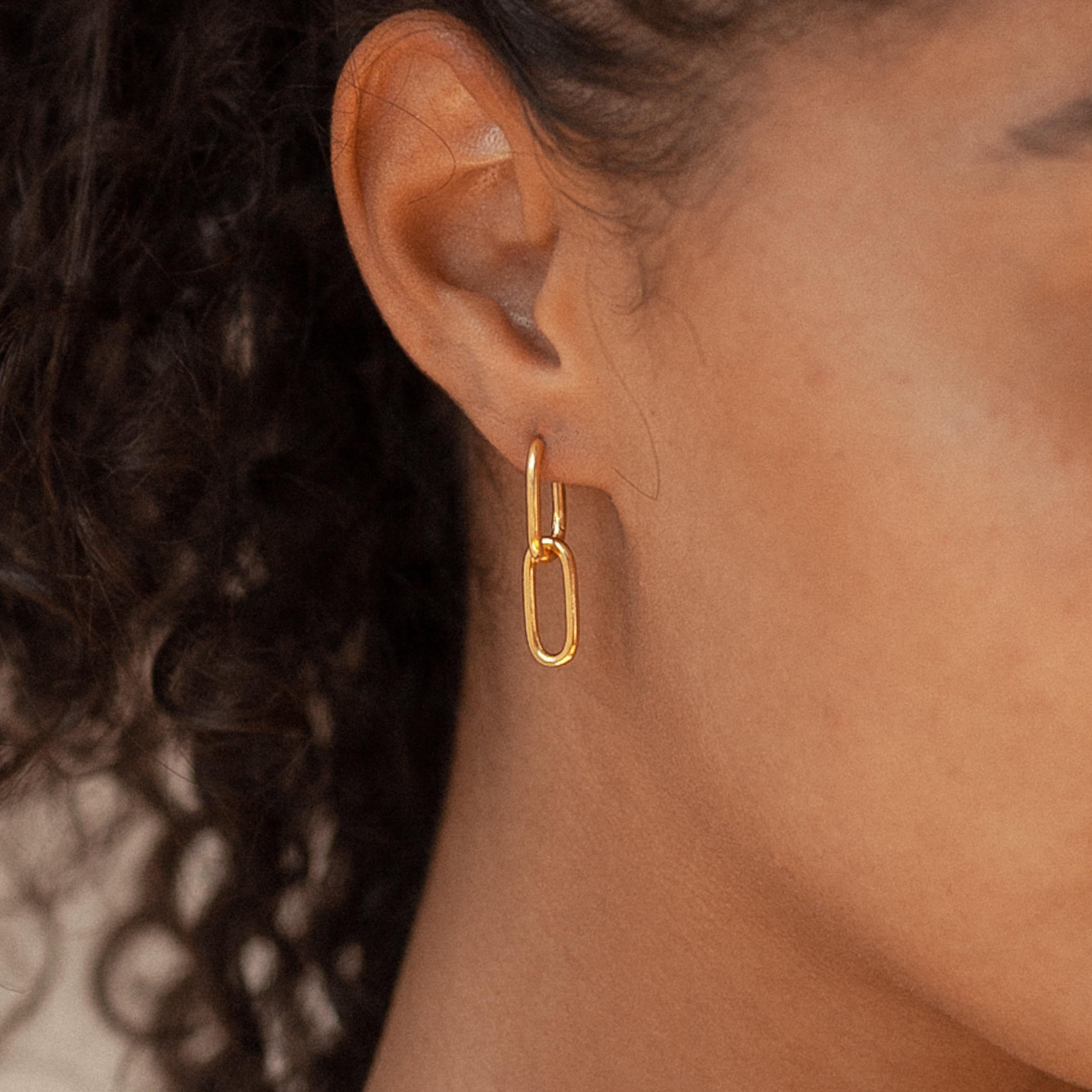 Close-up of a person wearing a gold rectangular link earring from the Linked Charm Necklace and Earrings Set in 18K Gold, with curly hair visible—an elegant choice for an anniversary gift.